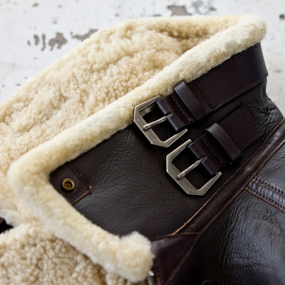 Close-up of the cream shearling aviator collar with two leather buckle straps.