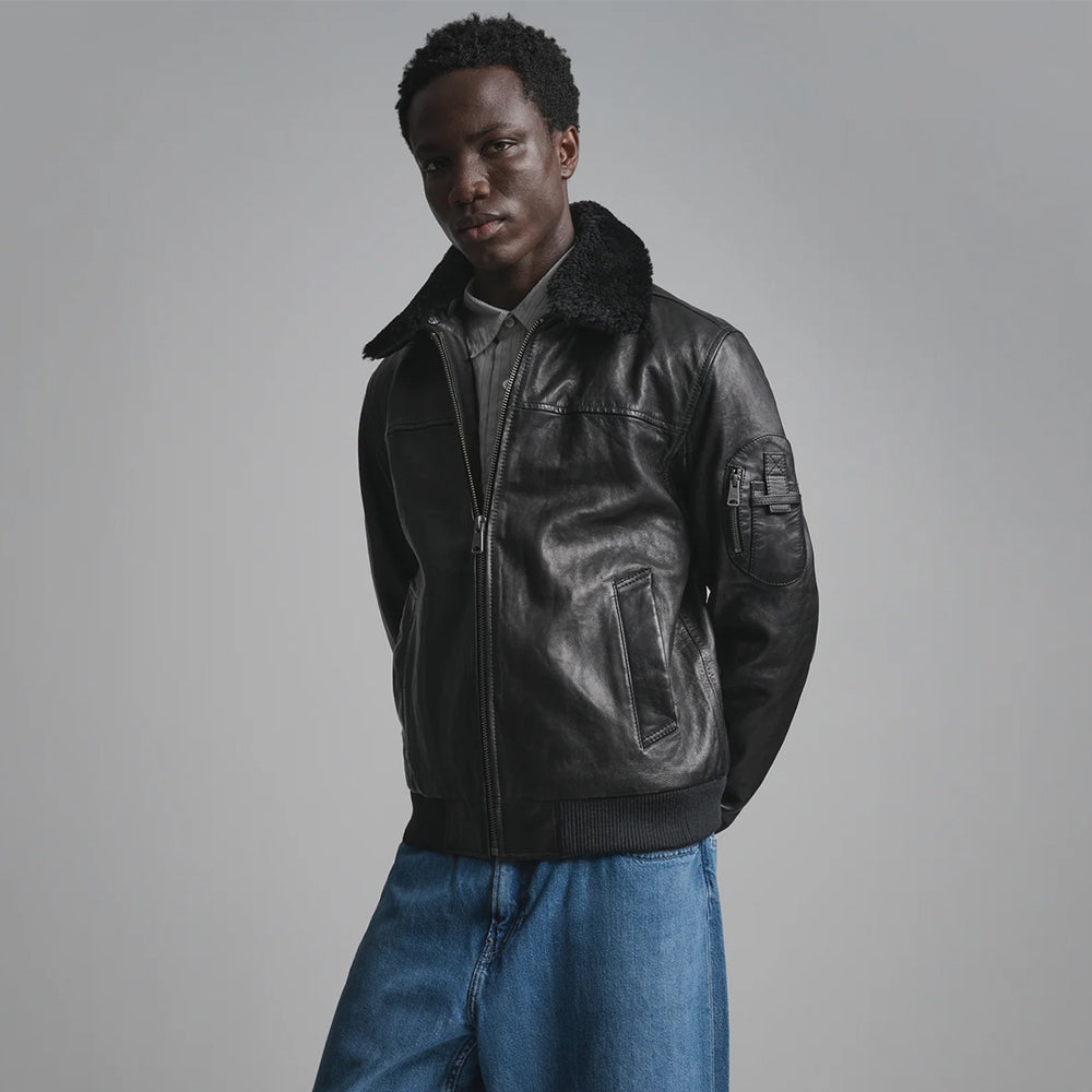 Black flight bomber showing zippered upper-arm utility patch with box-X reinforced leather tabs