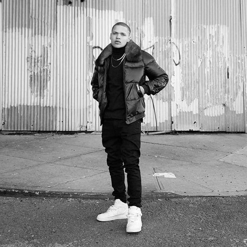 Man styling a black leather down bomber with dark clothing and white sneakers in an urban winter setting.