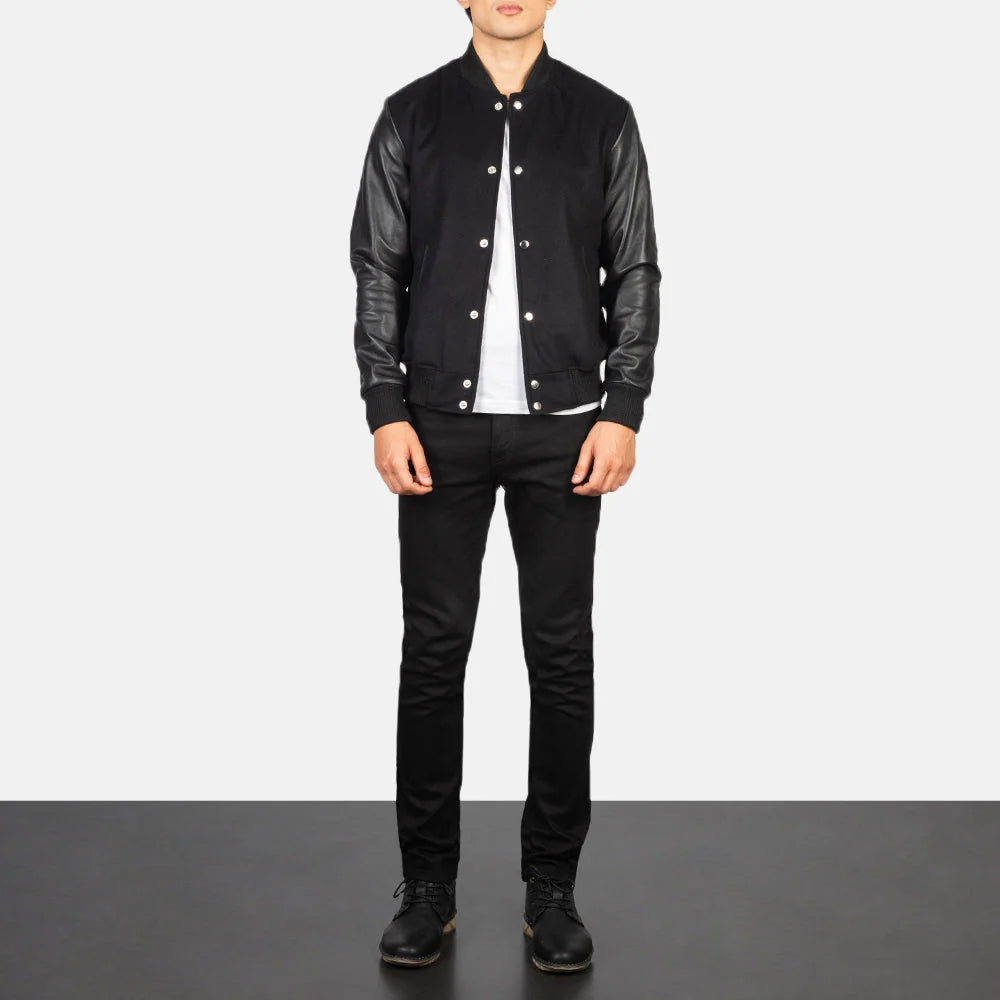 Full-body view of a man wearing an open black letterman jacket with genuine leather sleeves