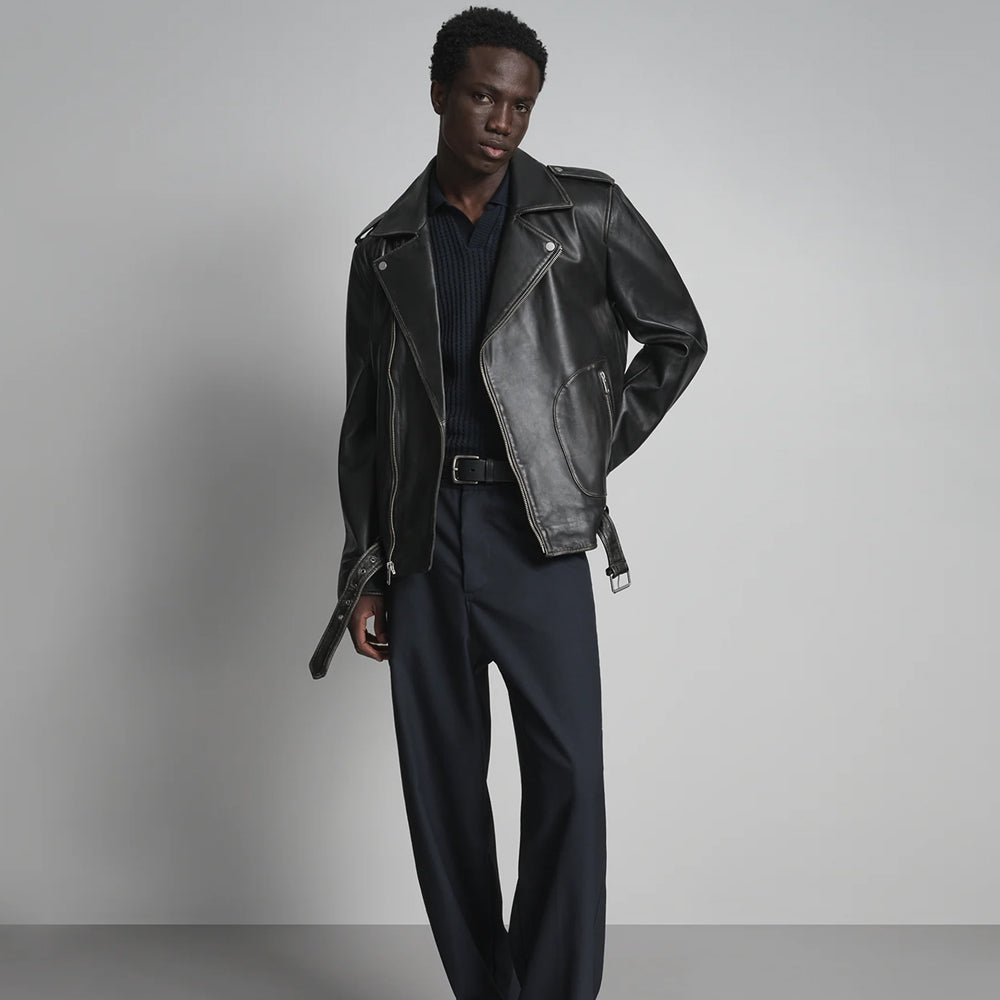 Full-length styling of men’s buckle-waist leather jacket worn open with extended belt ends and tailored trousers