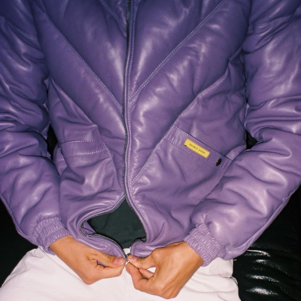 Lifestyle detail of a man fastening the center zipper on a lavender chevron-quilted leather puffer jacket