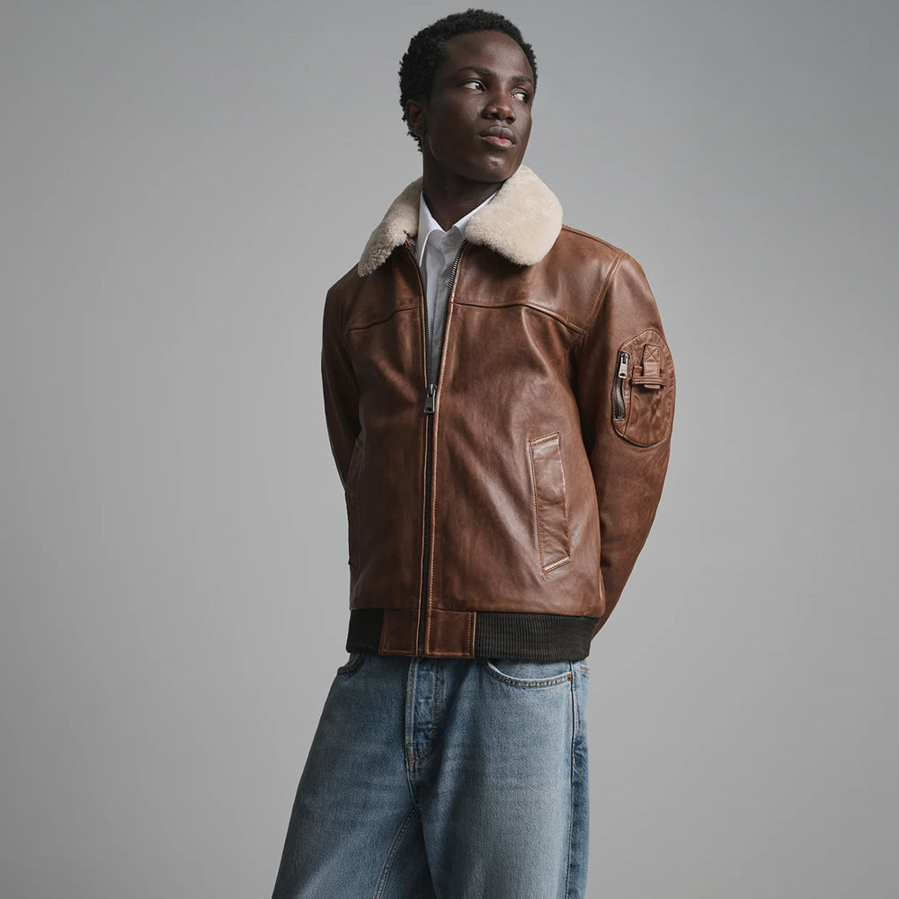 Men’s brown shearling-collar bomber with upper-sleeve zip utility pocket and angled welt hand pocket