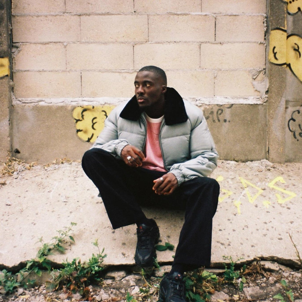 Man wearing the light grey Double Goose puffer bomber with black sheep-wool collar in an urban setting