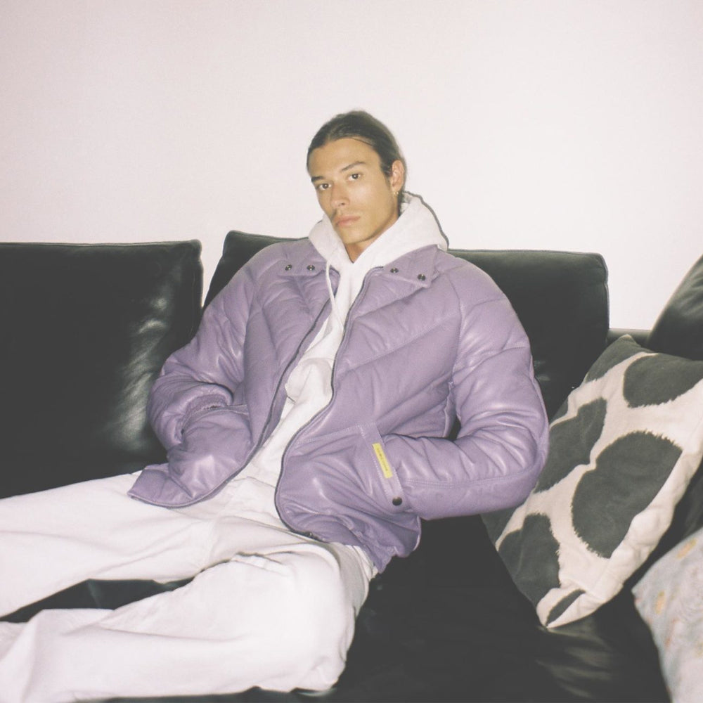 Man styling a lilac leather V-Bomber over a white hoodie and trousers in a relaxed streetwear outfit