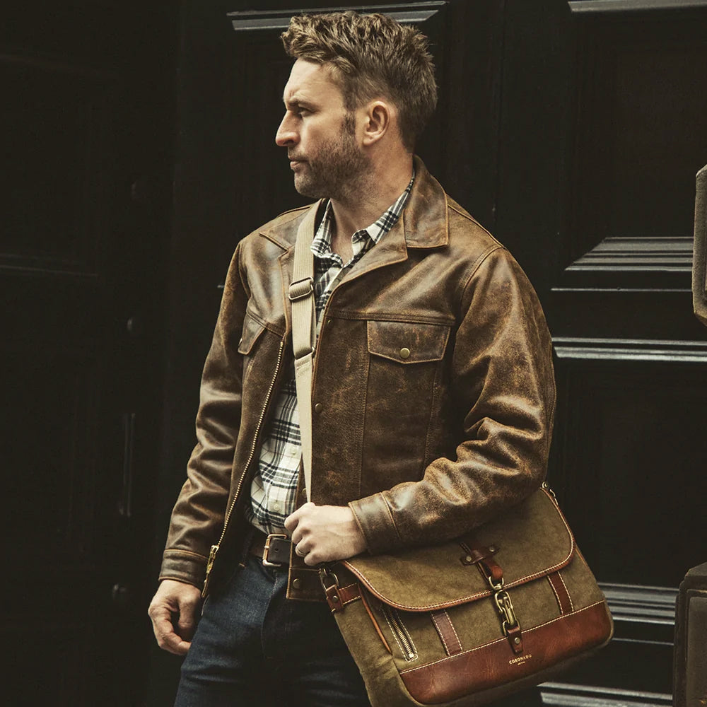 Man wearing a tobacco brown leather jean jacket with a plaid shirt and heritage messenger bag