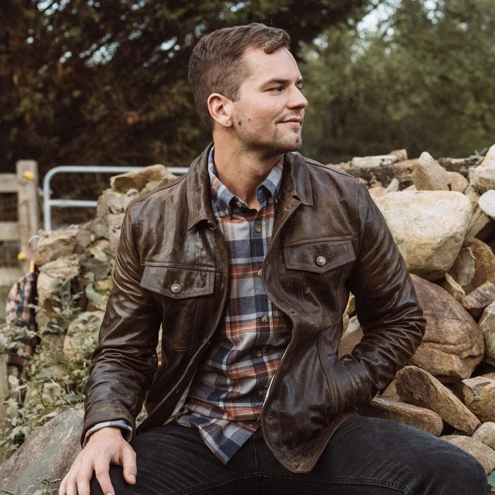 Man wearing a vintage brown leather jean jacket over a plaid shirt