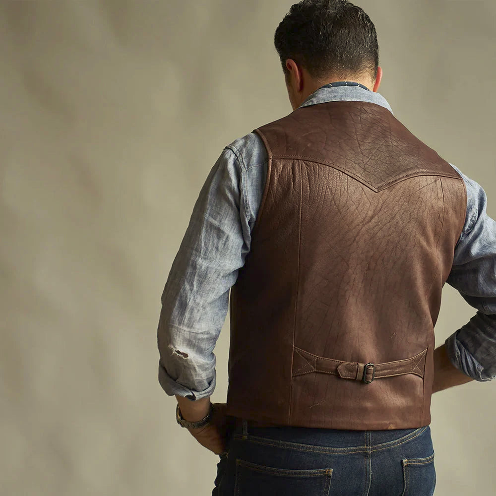 Modeled rear view of brown ranchwear leather vest showing pointed yoke and brass-buckle waist adjuster