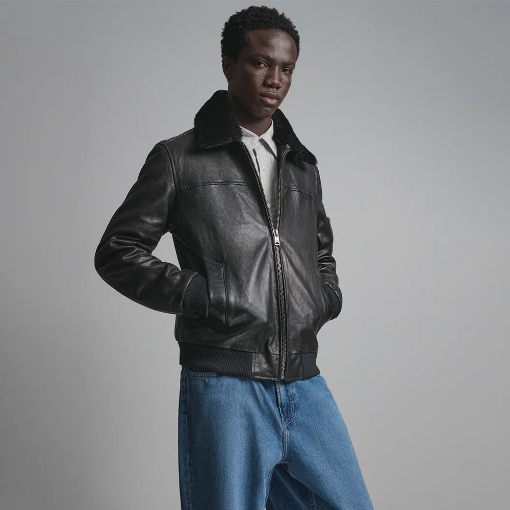 Three-quarter view of tonal black leather bomber with angled welt pockets, ribbed cuffs and waist trim