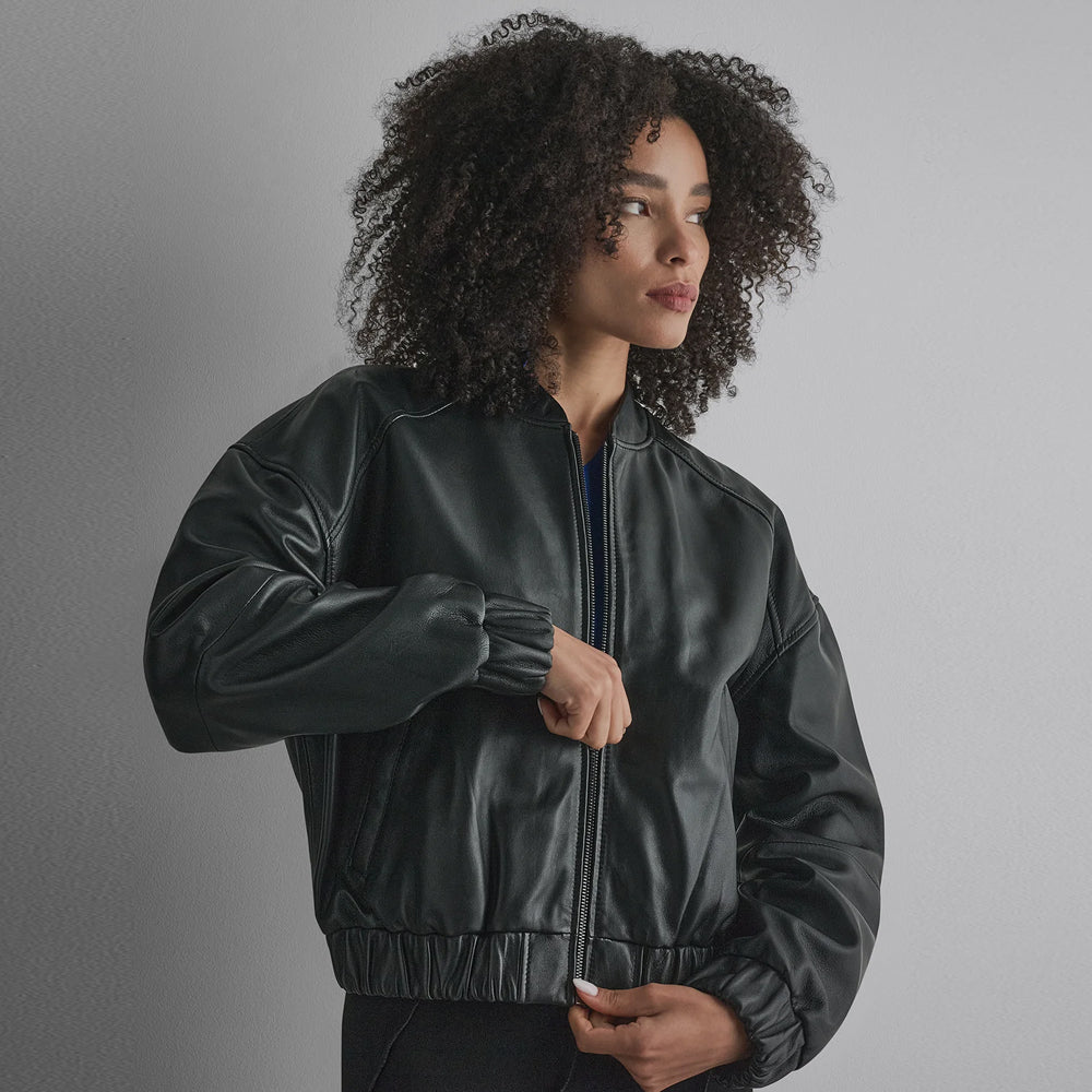 Close front view of a women’s black cropped sheep leather bomber with stand collar, dropped shoulders and gathered trims.