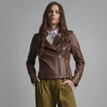 Front view of female model wearing a medium-brown asymmetrical leather biker jacket with closed zipper.