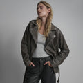Female model wearing an oversized charcoal-grey distressed leather biker jacket with lace-up sleeves and grey tank.