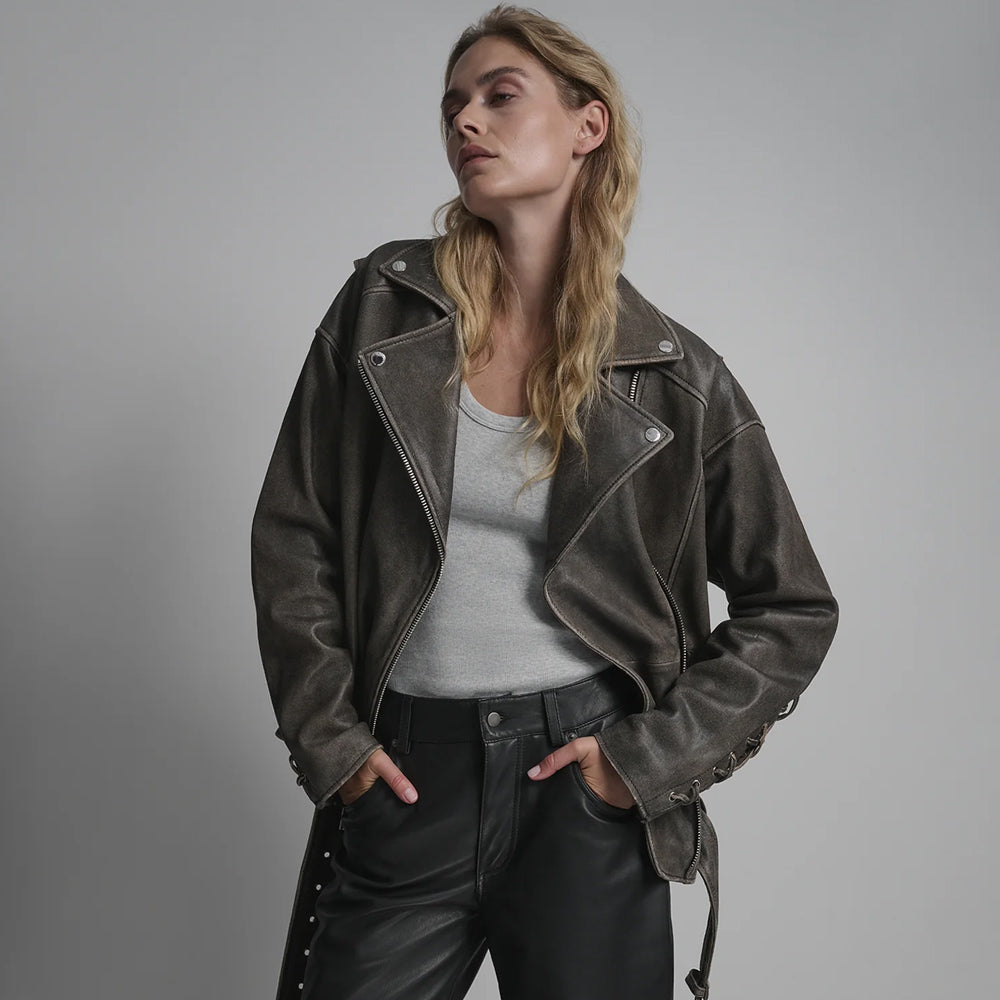 Female model wearing an oversized charcoal-grey distressed leather biker jacket with lace-up sleeves and grey tank.